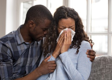 woman cries into tissue as husband comforts